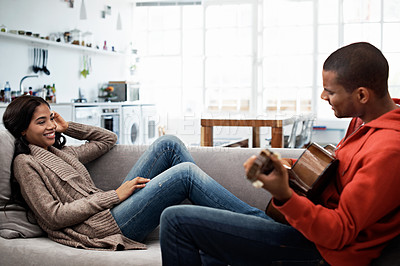 Buy stock photo Shot of a young man playing the guitar while relaxing on the sofa with his wife