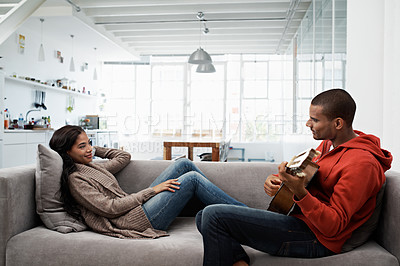 Buy stock photo Shot of a young man playing the guitar while relaxing on the sofa with his wife