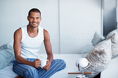 Buy stock photo Cropped portrait of a young man drinking coffee while sittng on his bed