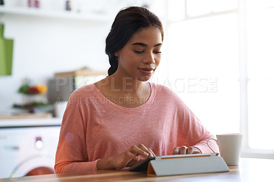 Buy stock photo Cropped shot of a young woman using her tablet in the kitchen