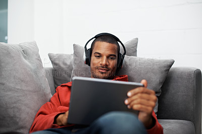 Buy stock photo Cropped shot of a young man listening to music on his tablet at home