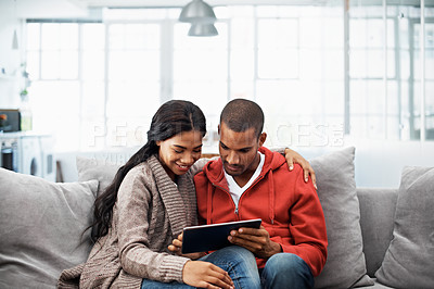 Buy stock photo Cropped shot of a young couple using their tablet while sitting on the sofa at home