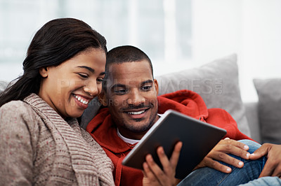 Buy stock photo Cropped shot of a young couple using their tablet while sitting on the sofa at home