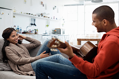 Buy stock photo Cropped shot of a young man playing guitar for his wife while relaxing on the sofa at home