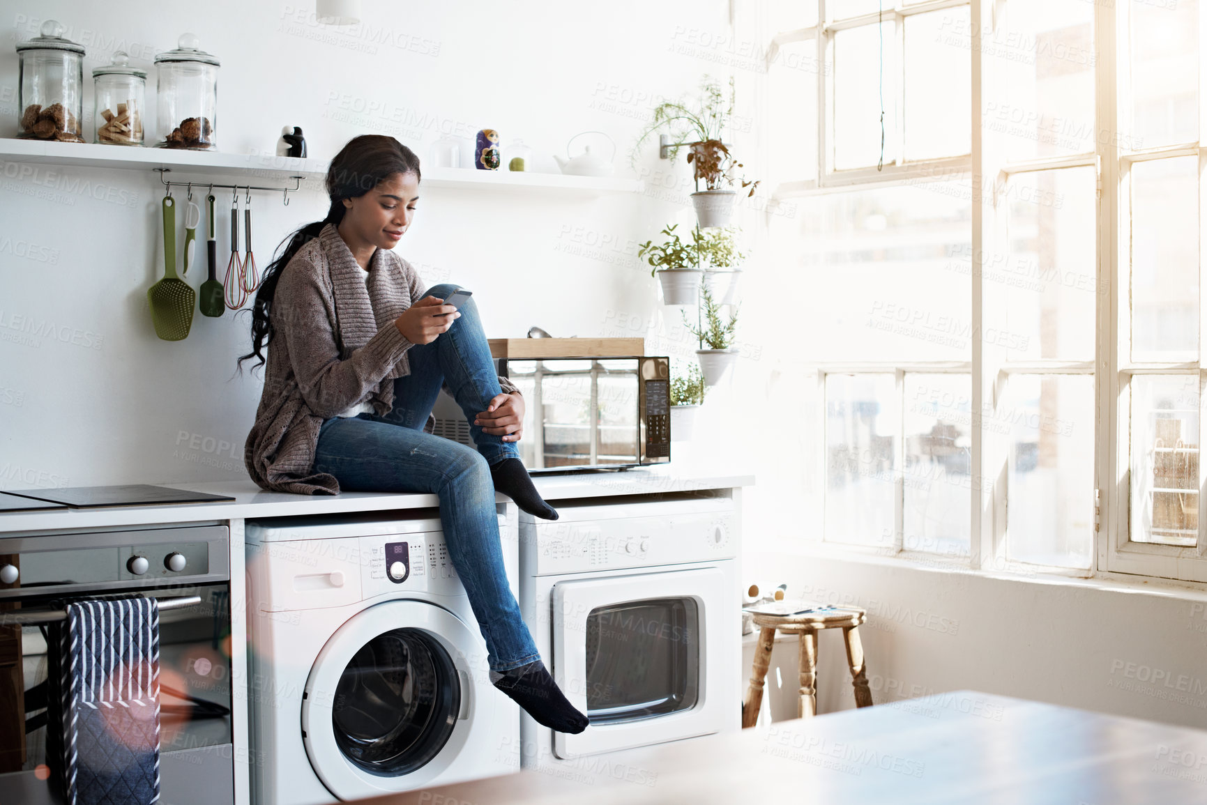 Buy stock photo Woman, relax and reading at house with phone, social media and comfortable for internet search. Smile, African person and rest in kitchen with mobile, browsing website and download ebook for me time