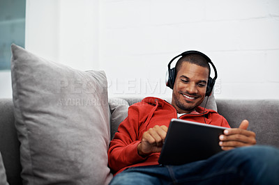 Buy stock photo Shot of a young man wearing headphones while using a digital tablet