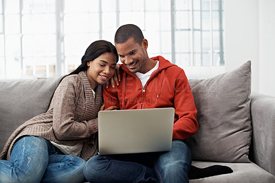 Buy stock photo Shot of a smiling young couple sitting on their sofa using a laptop