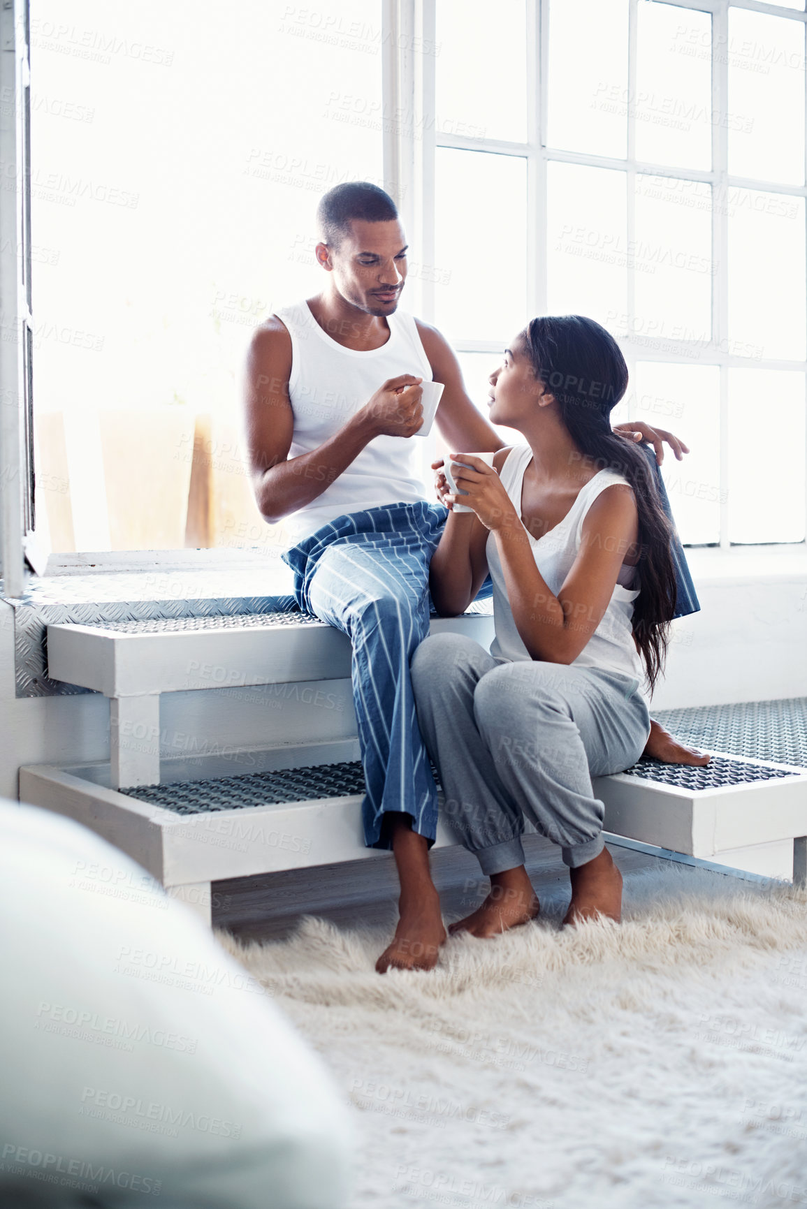 Buy stock photo Shot of a young couple talking together and drinking coffee while sitting in their bedroom