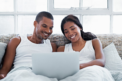 Buy stock photo Shot of a young couple lying in bed using a laptop