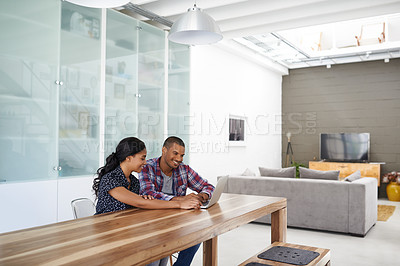Buy stock photo Shot of a young couple sitting at their dining table using a latpop