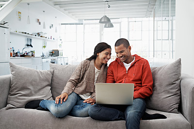 Buy stock photo Shot of a smiling young couple sitting on their sofa using a laptop