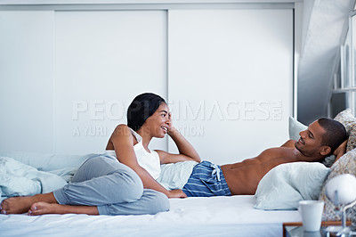 Buy stock photo Shot of a happy young couple talking together while lying in bed