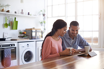 Buy stock photo Shot of a young couple drinking coffee and using their tablet in the kitchen