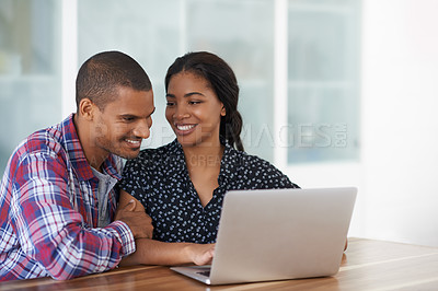 Buy stock photo Shot of a young couple sitting at their dining table using a latpop