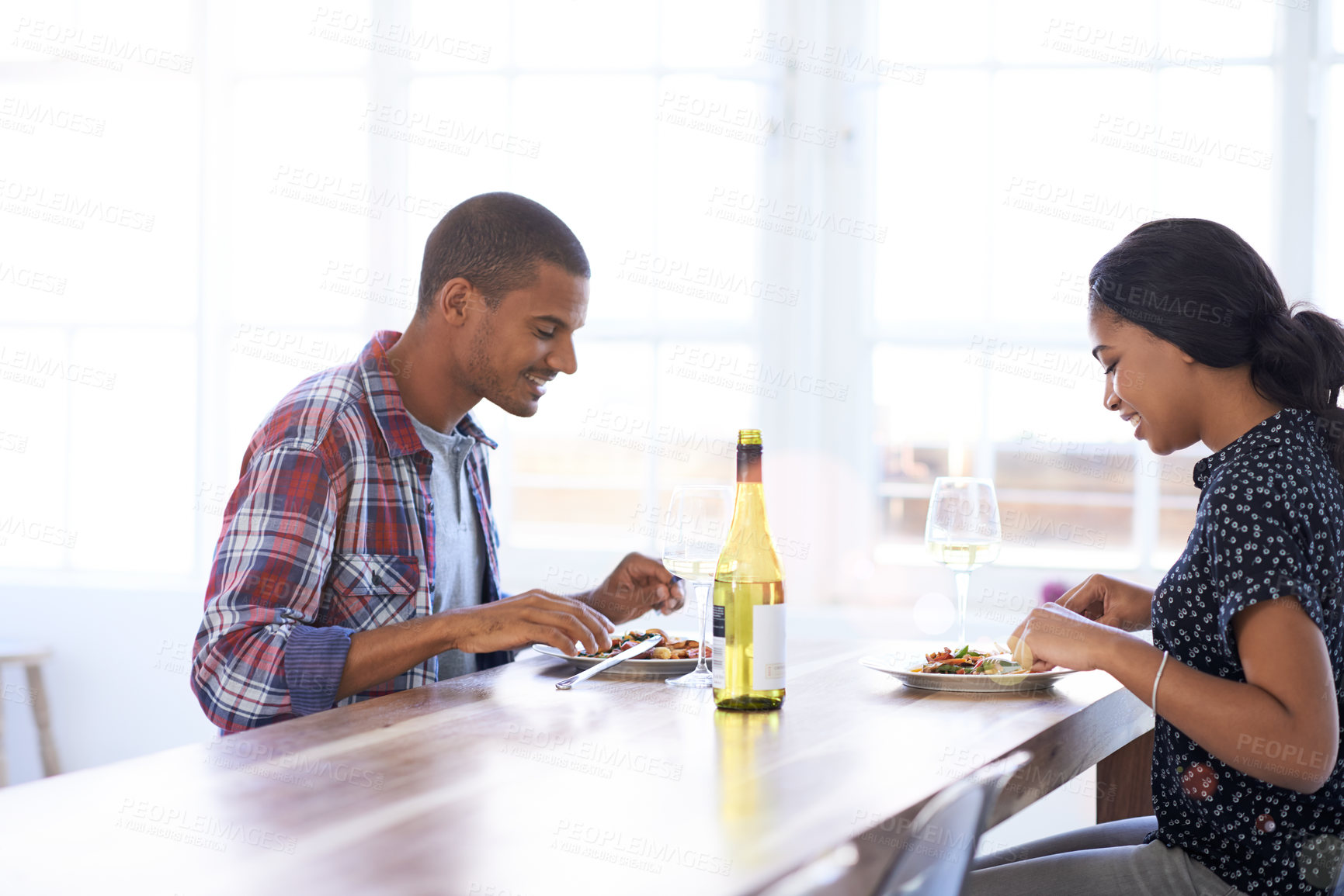 Buy stock photo Happy couple, eating and talking at dinner in home, meal together or relax with food and wine. Woman, man and supper with drinks in kitchen for bonding, hungry and conversation in house with dining
