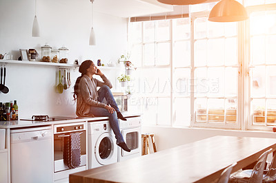 Buy stock photo Shot of a young woman sitting on her kitchen counter talking on the phone