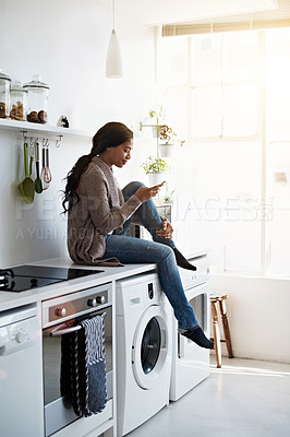 Buy stock photo Shot of a young woman sitting on her kitchen counter using the phone