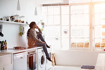 Buy stock photo Shot of a young woman sitting on her kitchen counter talking on the phone