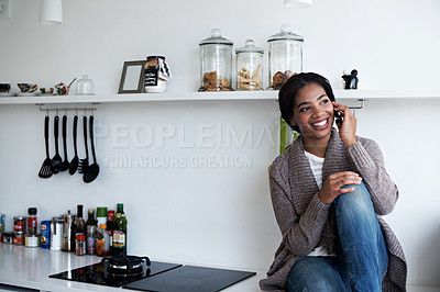 Buy stock photo Shot of a young woman sitting on her kitchen counter talking on the phone
