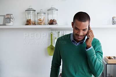 Buy stock photo Shot of a young man talking on his cellphone in the kitchen