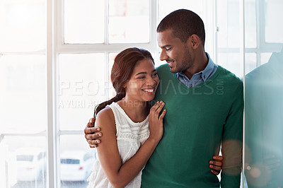 Buy stock photo Shot of an affectionate young couple standing arm in arm in their home
