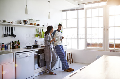 Buy stock photo Shot of a young couple talking together and drinking coffee in their kitchen in the morning