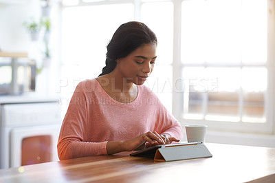 Buy stock photo Shot of a young woman using her tablet in the kitchen while drinking a coffee