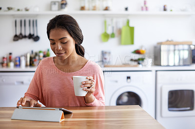 Buy stock photo Shot of a young woman using her tablet in the kitchen