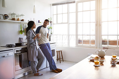 Buy stock photo Shot of a young couple talking together and drinking coffee in their kitchen in the morning