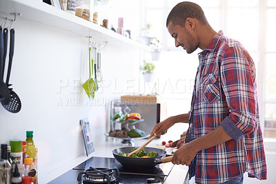 Buy stock photo Shot of a young man cooking over a stove in his kitchen