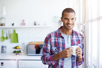 Buy stock photo Portrait of a smiling young man standing by his kitchen window drinking a coffee