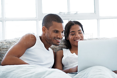 Buy stock photo Shot of a smiling young couple lying in bed using a laptop