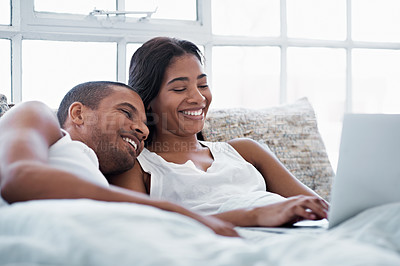 Buy stock photo Shot of a smiling young couple lying in bed using a laptop