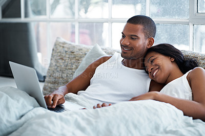 Buy stock photo Shot of a smiling young couple lying in bed using a laptop