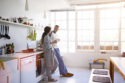Buy stock photo Shot of a young couple talking together and drinking coffee in their kitchen in the morning