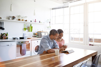 Buy stock photo Shot of a young couple drinking coffee and using their tablet in the kitchen
