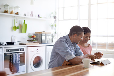 Buy stock photo Shot of a young couple drinking coffee and using their tablet in the kitchen