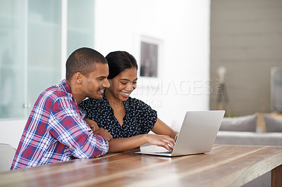 Buy stock photo Shot of a young couple sitting at their dining table using a latpop