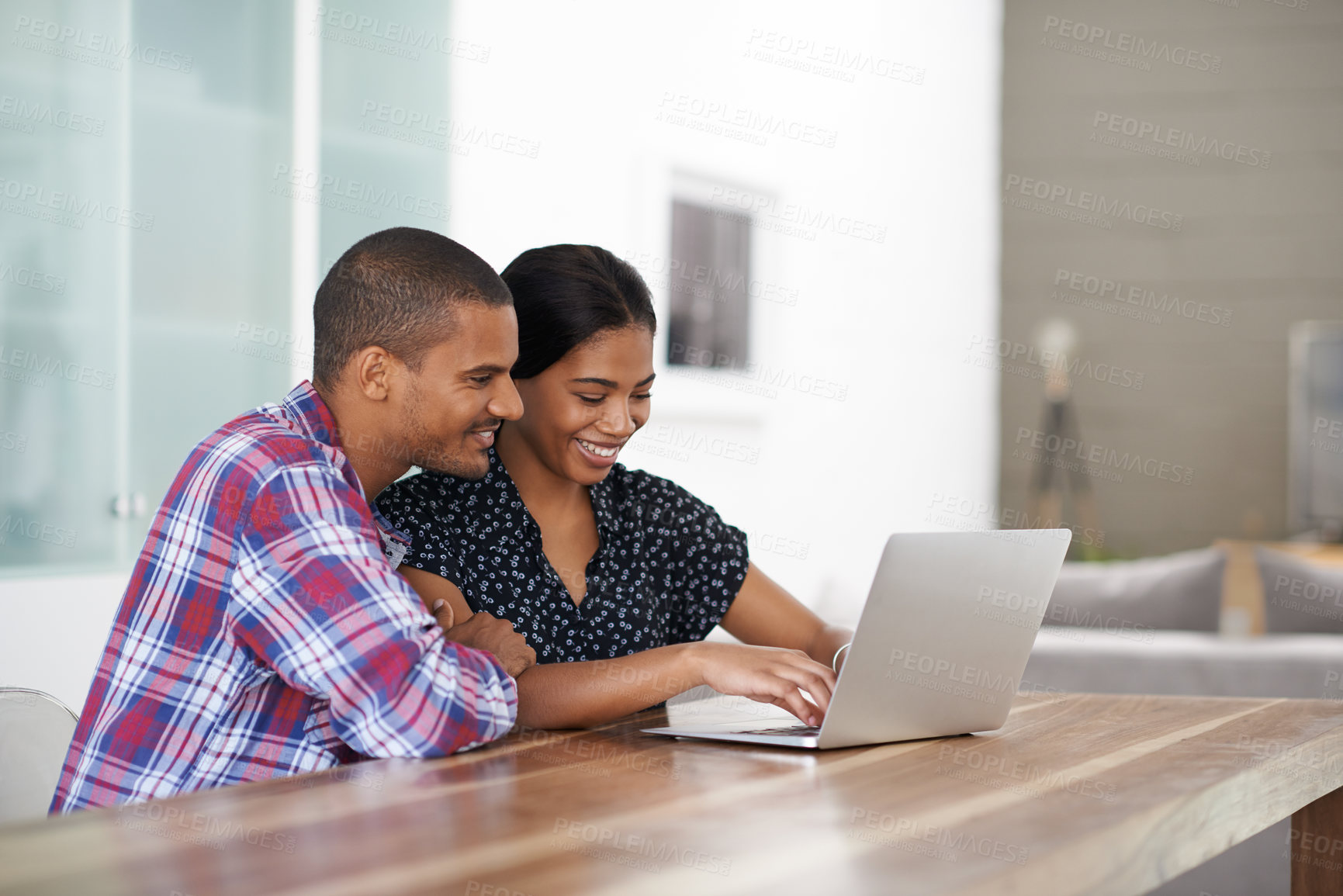 Buy stock photo Shot of a young couple sitting at their dining table using a latpop