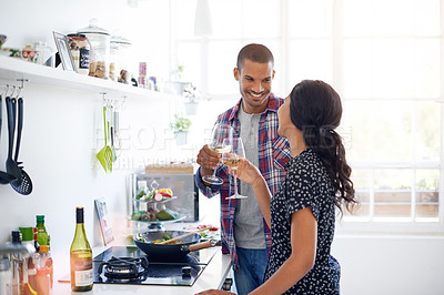 Buy stock photo Shot of a young couple toasting with wine while preparing dinner in their kitchen