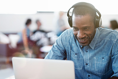 Buy stock photo Shot of a man wearing headphones and working on a laptop in an office with colleagues in the background
