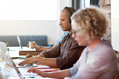 Buy stock photo Shot of people sitting in a row at a table in an office working on laptops