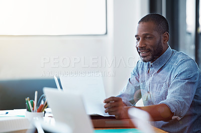 Buy stock photo Shot of a smiling man sitting at his desk in an office reading paperwork