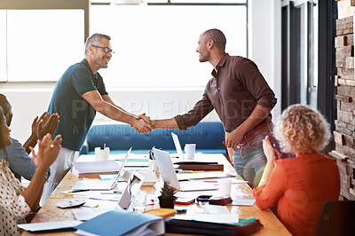 Buy stock photo Shot of two colleagues shaking hands together over a boardroom table while colleagues look on