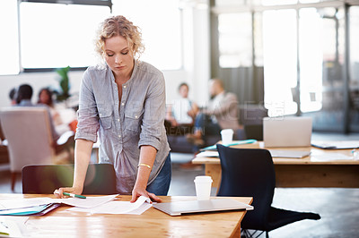 Buy stock photo Shot of a young businesswoman reading through some paperwork in her office