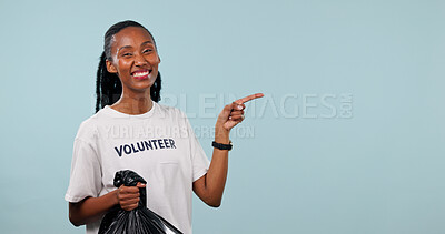 Buy stock photo Pointing, black woman and portrait of charity worker in studio by space for marketing of ngo service. Happy, trash bag and volunteer on blue background with advertising, options or donation guide.