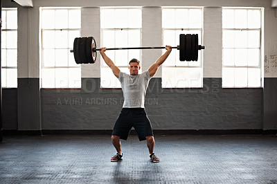 Buy stock photo Shot of a muscular young man in a gym lifting a barbell over his head