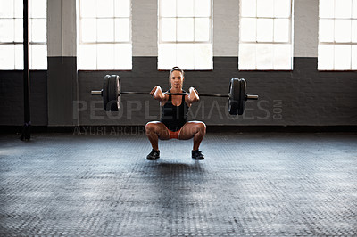 Buy stock photo Portrait of a muscular young woman in a gym doing squats while holding a barbell