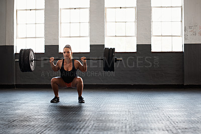 Buy stock photo Shot of a muscular young woman in a gym doing squats while holding a barbell