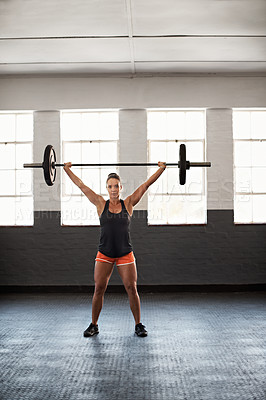 Buy stock photo Shot of a muscular young woman in gym holding a barbell over her head